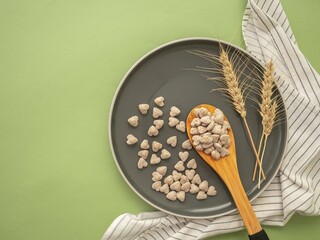 Extruded heart-shaped bran in a wooden spoon on a gray round plate. Spikelets of wheat, striped...