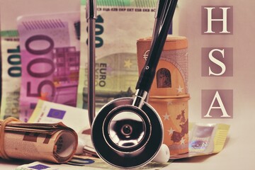 Wooden blocks with the word HSA standing for Health savings account put on Euro bills. Healthcare,...