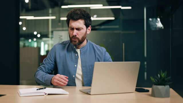 Sick businessman typing message on pc while having severe pain in pancreas and sitting in workspace. Stressed adult male problems having problems with digestion due to unhealthy lunch breaks.