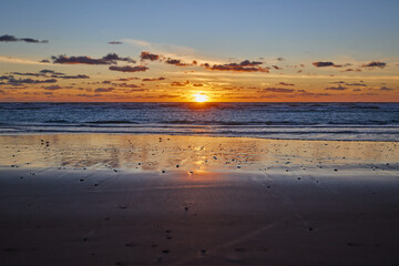 Dramatic sea sunset. The setting sun sinks into the sea. Calm waves roll onto the sandy beach.