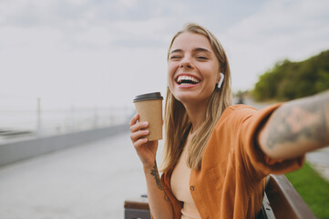 Young woman wear orange shirt casual clothes listen music in earphones do selfie shot on mobile...