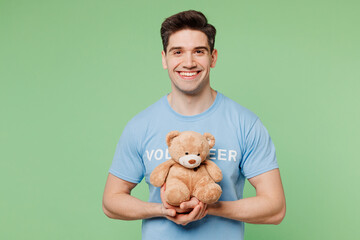 Young man wears blue t-shirt white title volunteer hold hug teddy bear plush toy look camera...