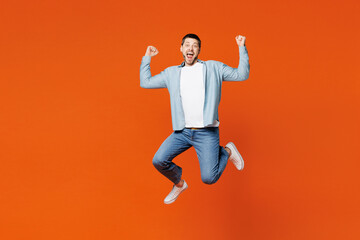 Fototapeta na wymiar Full body young overjoyed excited man wears blue shirt white t-shirt casual clothes jump high do winner gesture look camera isolated on plain red orange background studio portrait. Lifestyle concept.