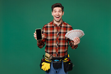 Young employee handyman man wears red shirt hold fan cash money in dollar banknotes mobile cell...