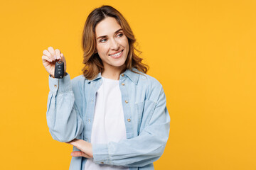 Young smiling happy woman she wears blue shirt white t-shirt casual clothes hold in hand car keys fob keyless system look aside on area isolated on plain yellow background studio. Lifestyle concept. - Powered by Adobe