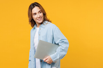 Obraz premium Side view young smart happy IT woman wearing blue shirt white t-shirt casual clothes hold closed laptop pc computer look aside isolated on plain yellow background studio portrait. Lifestyle concept.