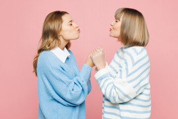 Side view elder parent mom 50s years old with young adult daughter two women together wear blue casual clothes hold hands together isolated on plain pastel light pink background. Family day concept.