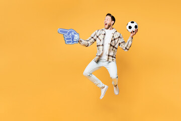 Fototapeta na wymiar Full body young man fan in casual clothes foam 1 fan glove finger up cheer up support football sport team hold in hand soccer ball watch tv live stream look aside isolated on plain yellow background