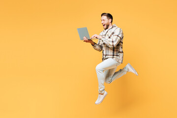Full body side view young Caucasian IT man wear brown shirt casual clothes jump high hold use work on laptop pc computer isolated on plain yellow orange background studio portrait. Lifestyle concept.