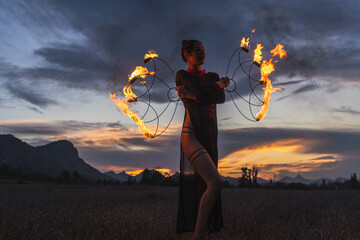 Woman dancing with fire fans with a sunset background