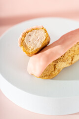 Eclair with strawberry custard cutaway and pink icing on pastel pink background. Delicious eclair...