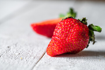 Several strawberries, some split, on a white wooden background, rich in fiber, combats constipation and regulates cholesterol, can cause allergies
