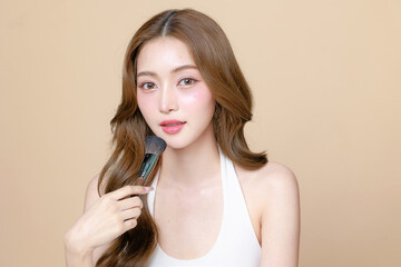 Young Asian beauty woman curly long hair with korean makeup style touch her face and perfect skin using brush on isolated beige background. Facial treatment, Cosmetology, plastic surgery.