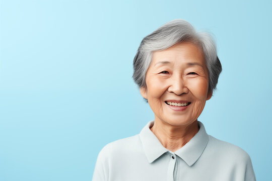 Portrait Of Older Chinese Woman Smiling Isolated On Solid Blue Background