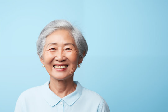 Portrait Of Older Chinese Woman Smiling Isolated On Solid Blue Background