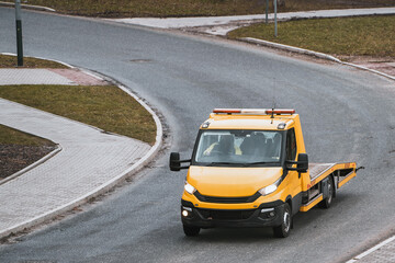 Top front view of an orange tow truck in an urban city street that has a flatbed and a winch. A...
