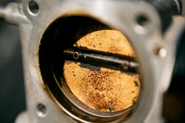 carbon deposits damage a throttle valve of a car engine. The valve blade is dirty and carbonized, which lowers the engine performance and efficiency. The air intake is reduced