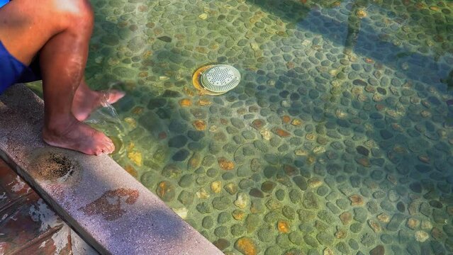 A man watching mobile during the hot spring bath in the seat of hot spring pool.Seat in the hot spring pool for sitting. .Tourists soak their feet in the hot spring pools to relax.