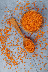 Photo of red lentils in wooden bowl with wooden measuring cup on wooden background.  Healthy lifestyle. Vegetarian and vegan diet.