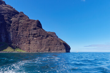 Magnificent cliff in the Pacific ocean and a small boat next to it view from a tourist boat at Napali Coast State Wilderness Park, Island of Kauai, Hawaii