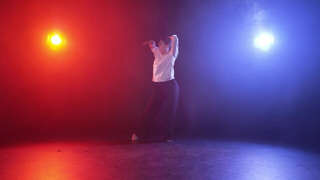 Young woman performing dance in studio. Expression girl dancing elegant contemporary in dance black studio in multi-colored red blue spotlights. Motion dance, female professional dancer concept.