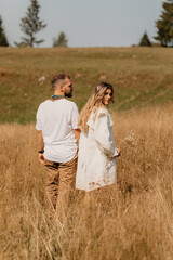 Outdoor shot of young couple in love walking on  through grass field in the mountain area