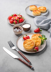 Cottage cheese, cheesecakes or syrniki with strawberries, sour cream, jam and mint leaves on a white plate on a light background with cutlery and napkin.