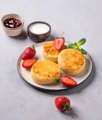 Cottage cheese, cheesecakes or syrniki with strawberries and mint leaves on a white plate on a light background with sour cream and berry jam.