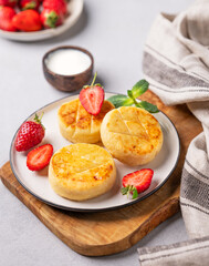 Cottage cheese, cheesecakes or syrniki with strawberries and mint leaves on a cutting board  on a light background with sour cream and napkin.