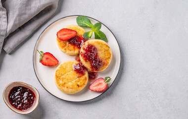 Cottage cheese, cheesecakes or syrniki  sprinkled berry sauce on a white plate  with strawberry on a light background with jam and napkin.