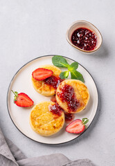 Cottage cheese, cheesecakes or syrniki  sprinkled berry sauce on a white plate  with strawberry on a light background with jam and napkin.
