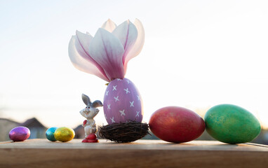 Composition with multi-colored Easter and chocolate eggs, an Easter bunny and a blooming large magnolia flower in backlight. good spring religious holiday