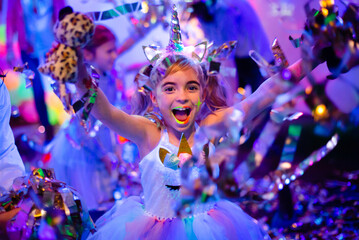 Happy girl with neon make-up in the Unicorn headband having fun with shiny paper confetti on her...