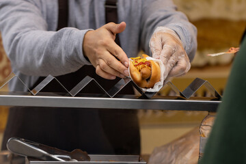 Unrecognizable cook selling a hot dog on the street - obrazy, fototapety, plakaty