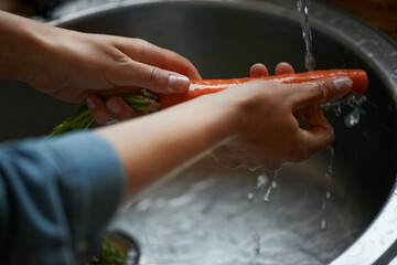 Hands, carrots and washing vegetables or healthy food in sink, preparing meal and kitchen while...