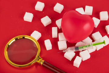 Broken heart made from sugar cubes and a syringe on a red background. Diabetes concept. View from...