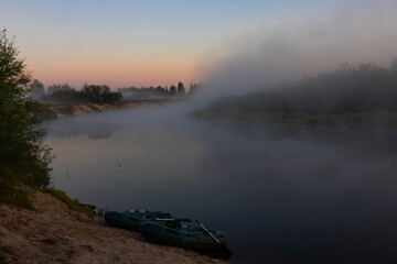 Two rubber boats with fishing tackle in the early morning during the fog, parked on the banks of the river.
