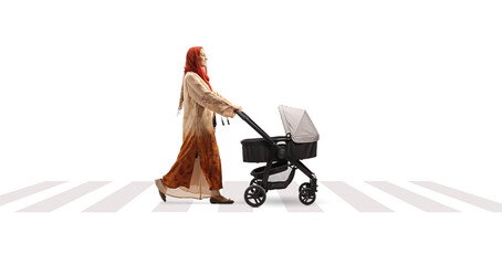 Full length profile shot of a woman wearing a hijab and pushing a baby stroller at a pedestrian...