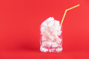 A glass of white glass with a straw filled with white cubes of refined sugar on a red background. Copy space.
