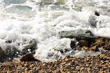 Beautiful background image of pebbles on the beach with waves and sea.