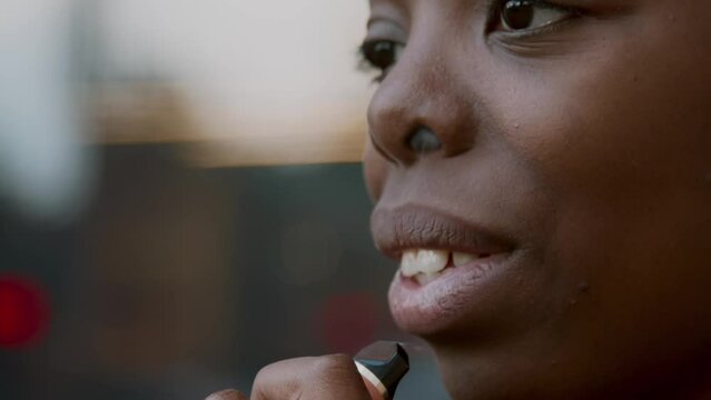 Close-up portrait shot footage of joyful young African American woman relaxing outdoors vaping e-cigarette looking away