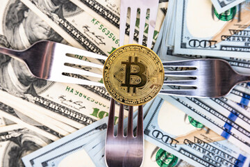 Gold bitcoin on the background of one hundred dollar bills and cutlery.