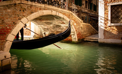 Fototapeta na wymiar Gondel fährt in Venedig unter einer Brücke auf dem Kanal in das Sonnen Morgenlicht.