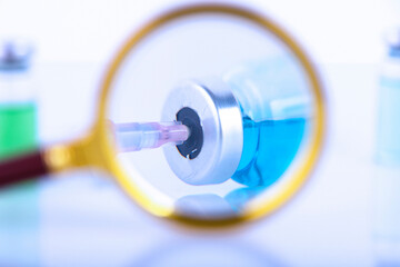 Vaccination concept. Magnifying glass with vial, dose, vaccine, antivirus, with syringe and needle, Selective focus. Copy space.