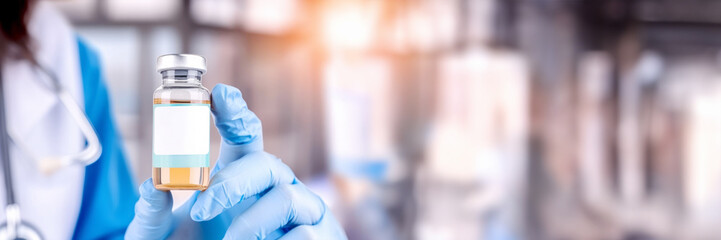 Banner with Doctor's hand holding a vaccine vial with white label mock-up for pharmaceutical ads, healthcare education, and vaccination awareness. Blurred hospital background with copy space for text - obrazy, fototapety, plakaty
