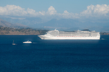 a cruise liner and two small yachts sail on the sea against the backdrop of mountains and sky