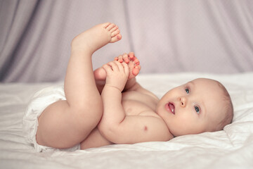 portrait of a happy seven month old baby lying on his back and playing with his leg