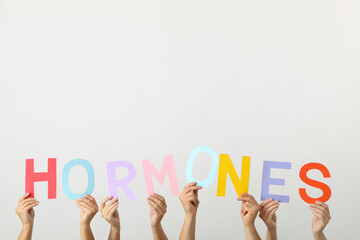 The word hormones in human hands, on a light background.