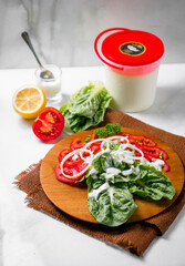 a wooden plate topped with a salad containing green leafy vegetables, sliced tomatoes, and red onion wedges with ranch dressing