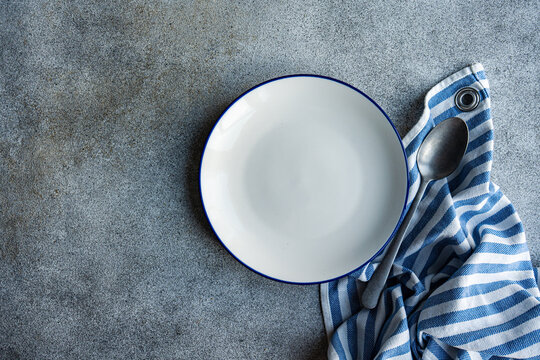 Overhead view of an empty plate with a striped napkin and spoon on a table